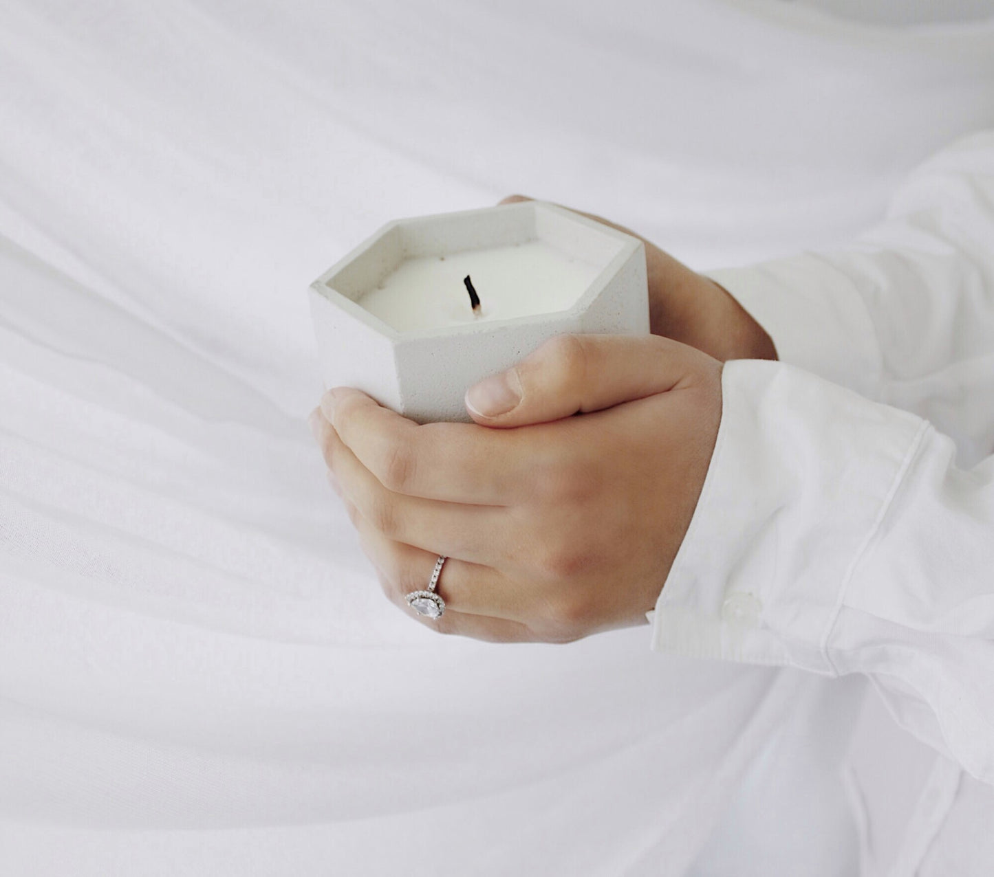 Hands holding hexagon white cement jar with candle. Made by Paige Soy Candles