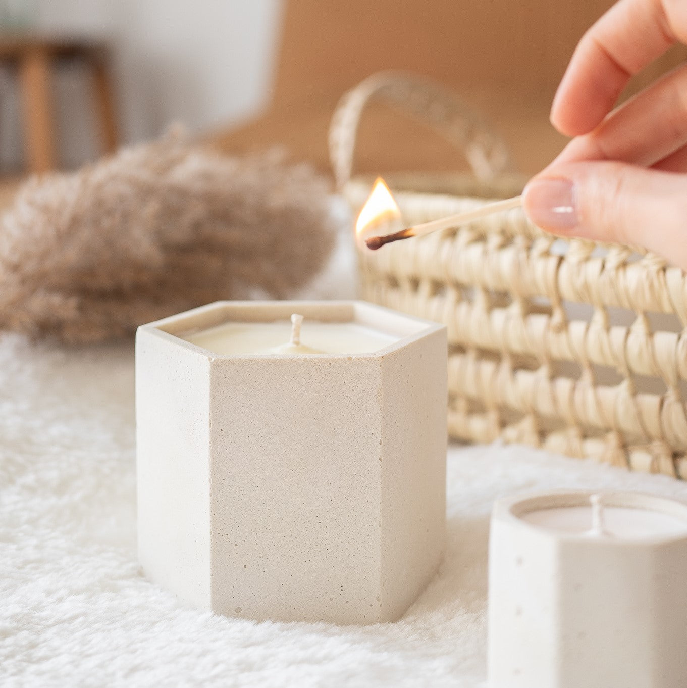 A hand is lighting a 9 ounce candle with a match. Candle is in a hand-made hexagonal white cement jar. Made by Paige Soy Candles