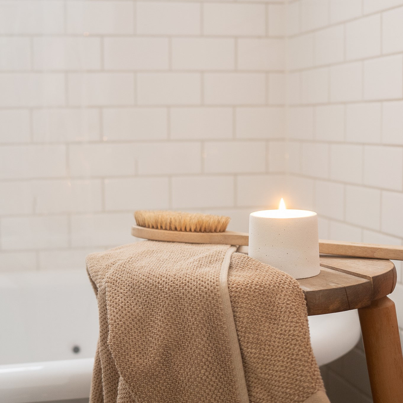 A lit 4 ounce candle on a bench. Jar holding candle is circular and hand-made with white cement. Made by Paige Soy Candles