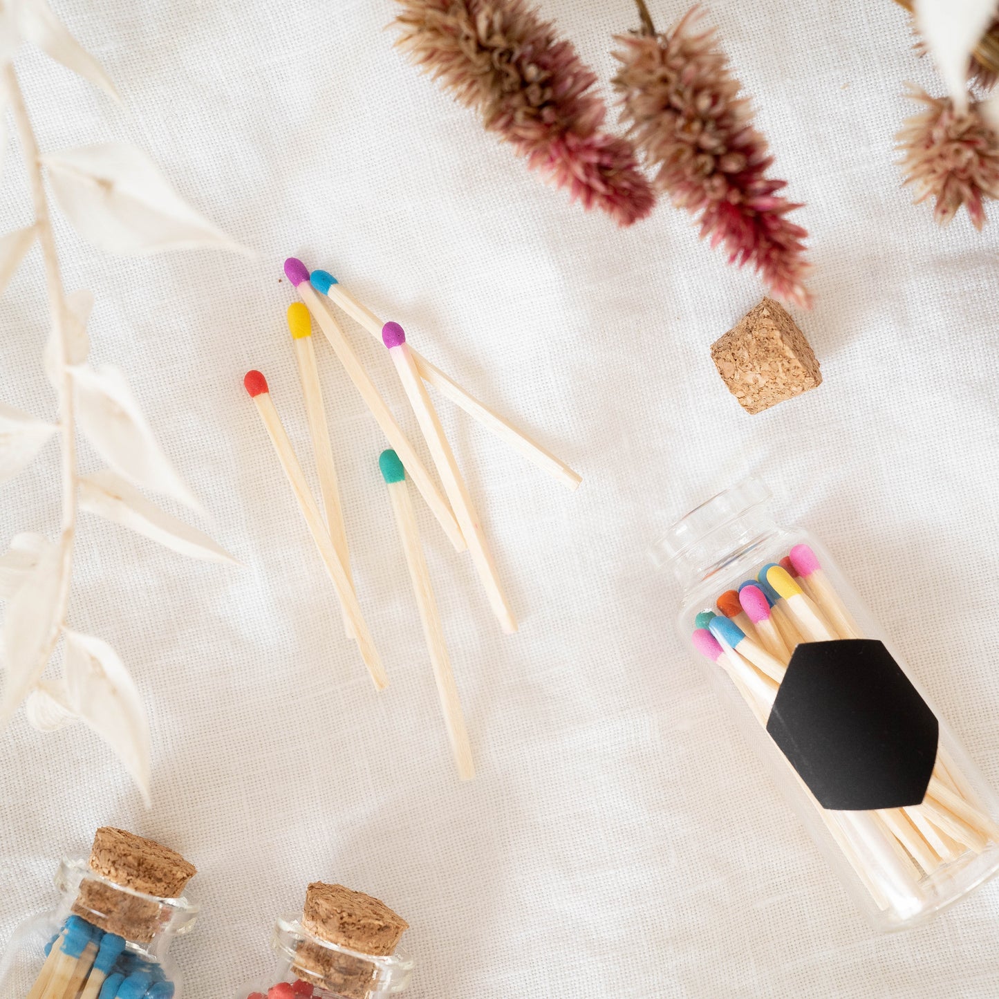 Colorful matches in a jar laying on a white background. Match bottle has a cork top, and hexagonal strike paper. Made by Paige Soy Candles