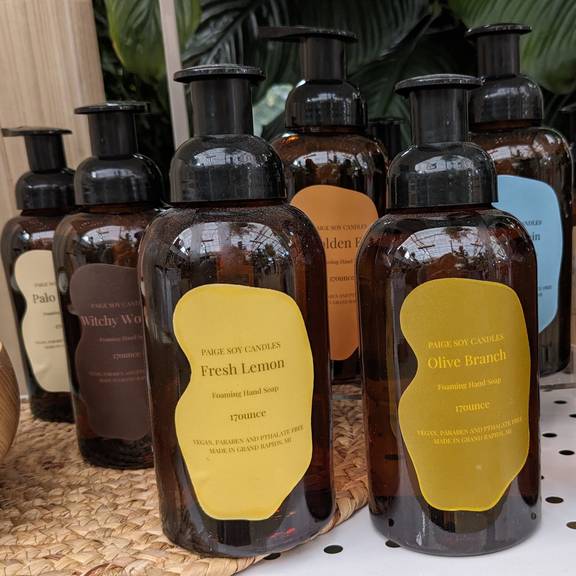 Foaming hand soap in dark amber bottles. Labels are brightly colored, and show scents Fresh Lemon, Olive Branch, Spring Rain, Golden Fig, Witchy Woman, and Palo Santo. Made by Paige Soy Candles