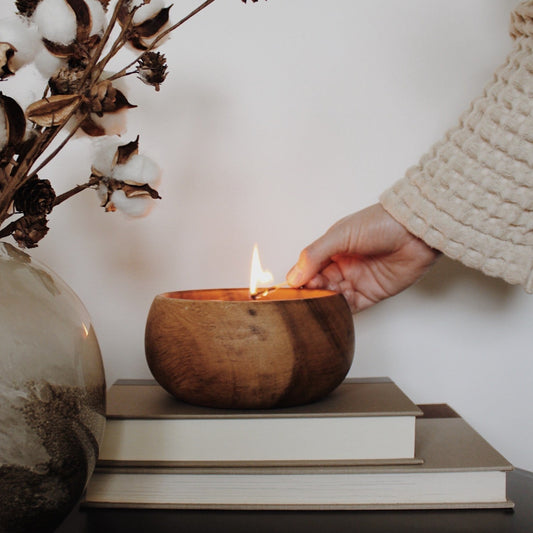 Hand holding match lighting wooden bowl candle. Made by Paige Soy Candles