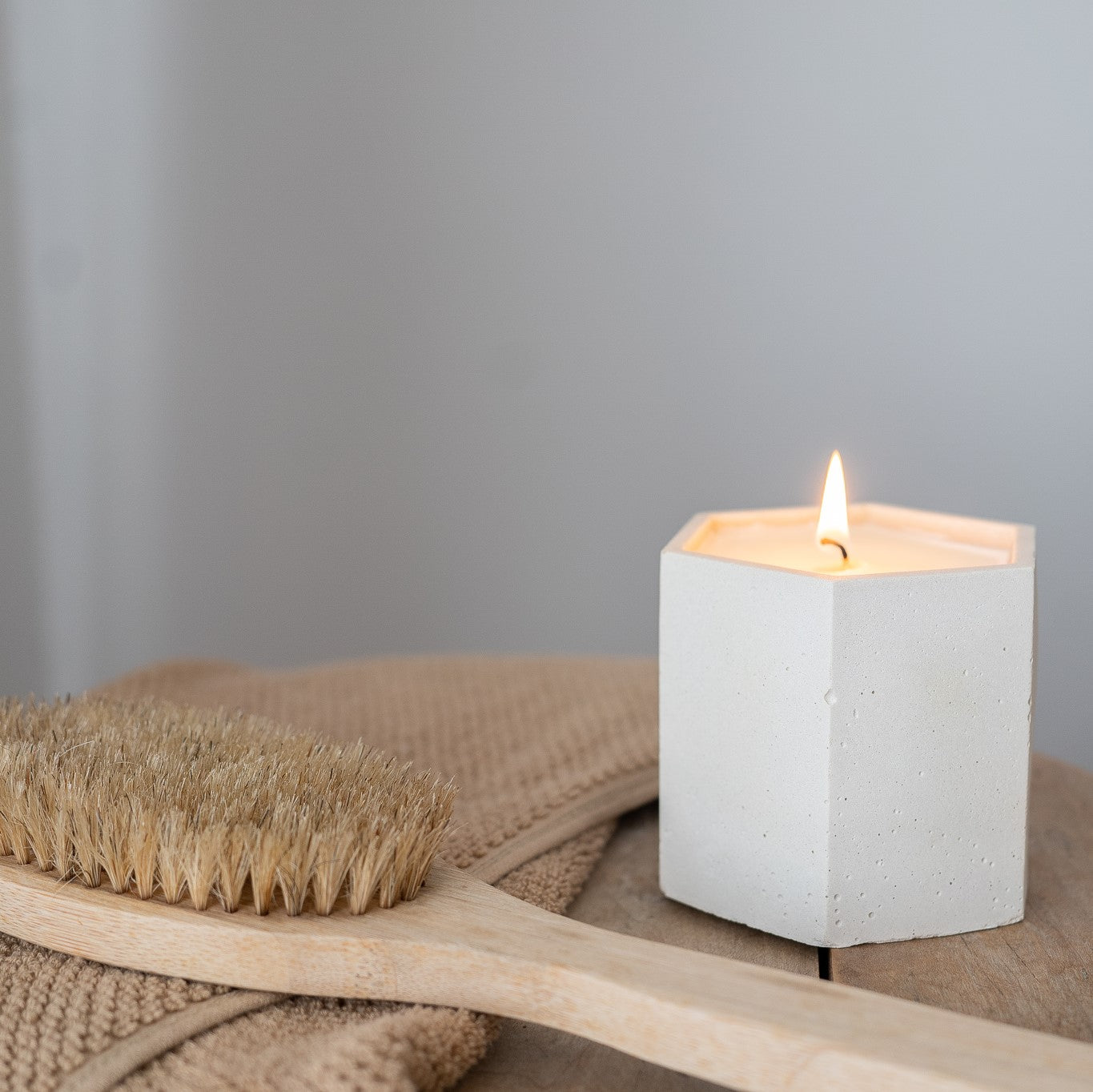 A lit 9 ounce candle sits on a bench. Candle is in a hand-made hexagonal white cement jar. Made by Paige Soy Candles