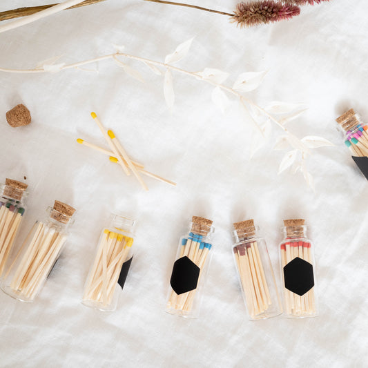 Colorful matches in bottles on a white background. Match bottles have cork tops, and hexagonal strike paper on the side. Made by Paige Soy Candles